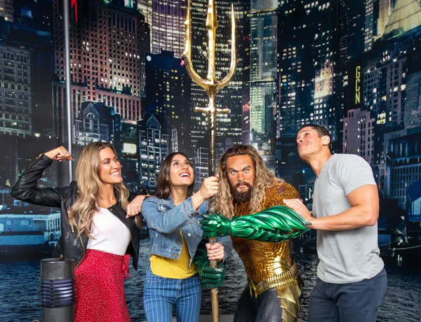 Three guests pose with Justice League’s Aquaman wax figure at Madame Tussauds Orlando, smiling excitedly.